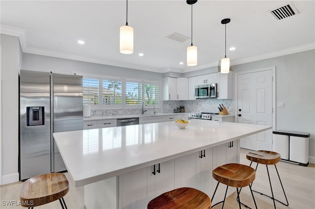 kitchen featuring pendant lighting, white cabinets, a kitchen breakfast bar, a kitchen island, and stainless steel appliances