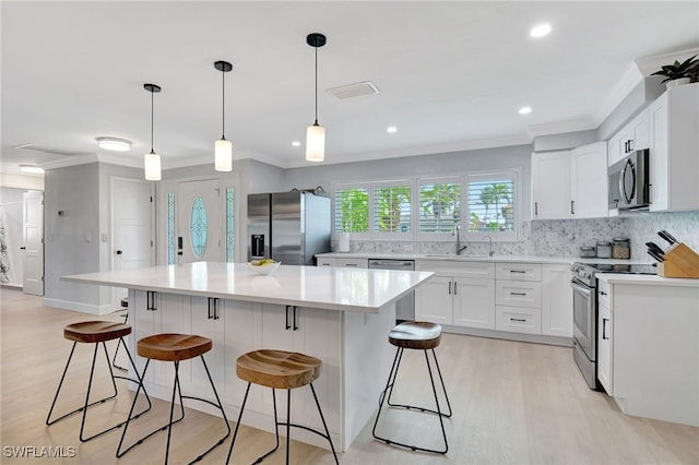 kitchen with white cabinetry, a center island, decorative light fixtures, appliances with stainless steel finishes, and light wood-type flooring