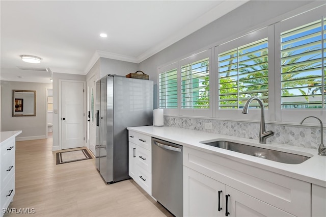 kitchen with appliances with stainless steel finishes, a sink, ornamental molding, light wood-style flooring, and light countertops