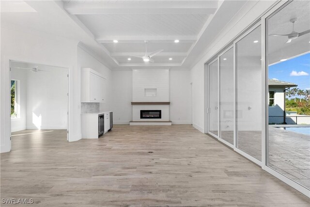 unfurnished living room with ceiling fan, plenty of natural light, beamed ceiling, and light wood-type flooring