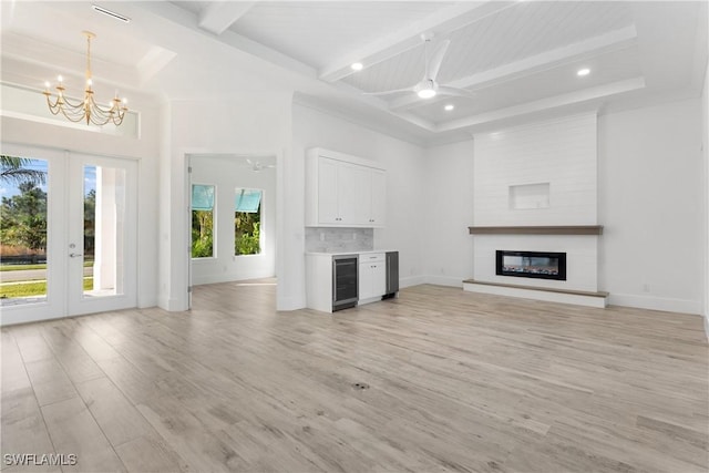 unfurnished living room featuring light hardwood / wood-style flooring, beam ceiling, wine cooler, a large fireplace, and ceiling fan with notable chandelier