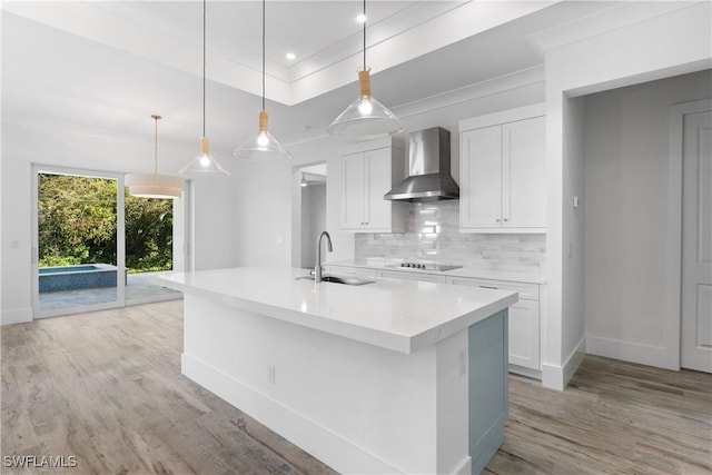 kitchen featuring pendant lighting, a kitchen island with sink, wall chimney range hood, and white cabinets