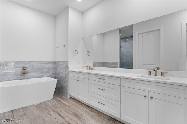 bathroom with hardwood / wood-style floors, vanity, a washtub, and tile walls