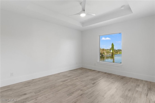 unfurnished room featuring a water view, ceiling fan, a tray ceiling, and light hardwood / wood-style floors