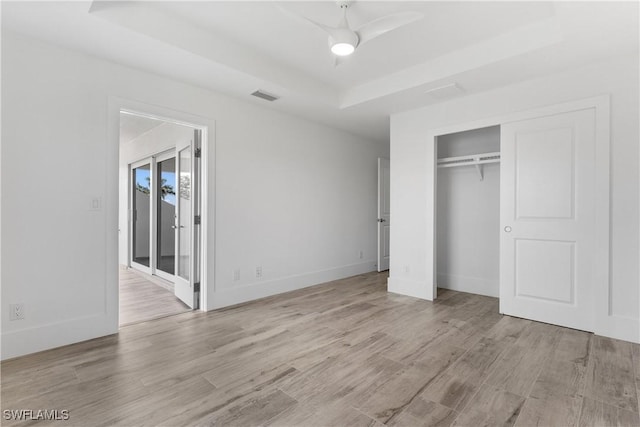 unfurnished bedroom with a closet, light hardwood / wood-style floors, ceiling fan, and a tray ceiling