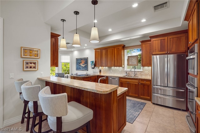 kitchen featuring sink, hanging light fixtures, stainless steel appliances, kitchen peninsula, and a breakfast bar area