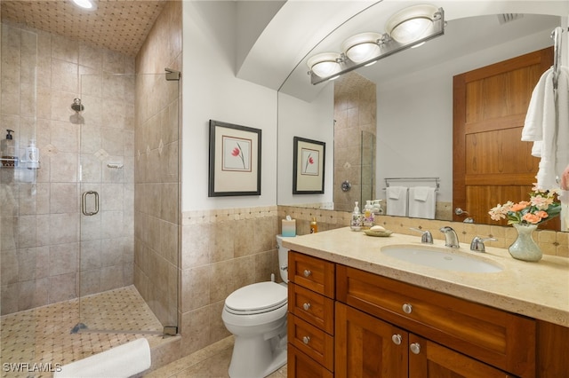 bathroom featuring tile patterned flooring, toilet, a shower with door, vanity, and tile walls