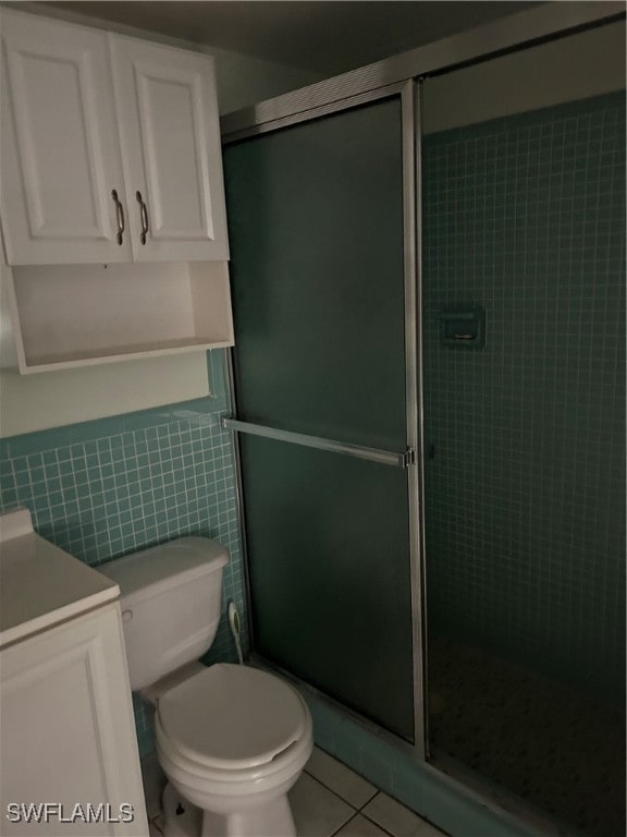 bathroom featuring vanity, a shower with door, tile patterned flooring, toilet, and tile walls