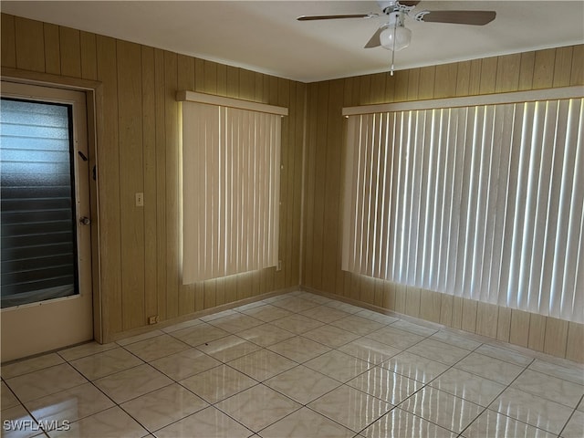 empty room with wooden walls, light tile patterned flooring, and ceiling fan