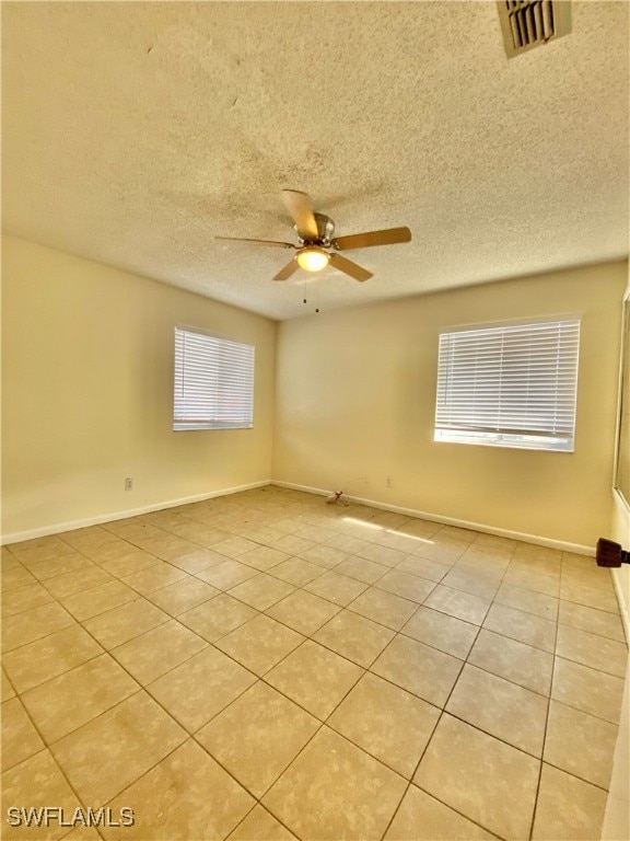 empty room featuring ceiling fan, plenty of natural light, light tile patterned flooring, and a textured ceiling