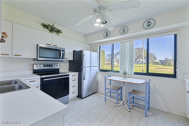 kitchen featuring appliances with stainless steel finishes, light wood-type flooring, a textured ceiling, sink, and white cabinets