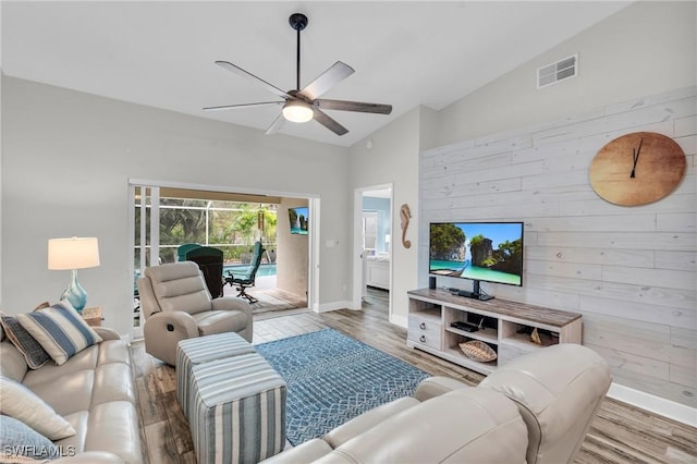 living room with lofted ceiling, wood-type flooring, wooden walls, and ceiling fan