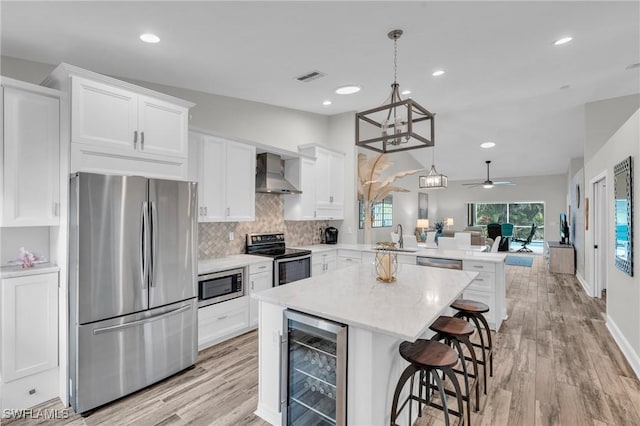 kitchen featuring wall chimney exhaust hood, decorative light fixtures, beverage cooler, white cabinetry, and appliances with stainless steel finishes