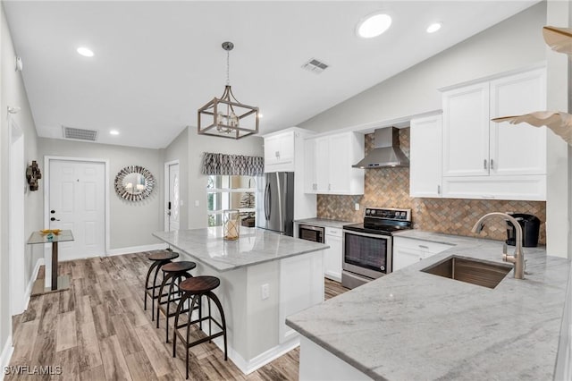 kitchen featuring light stone countertops, vaulted ceiling, stainless steel appliances, wall chimney range hood, and sink