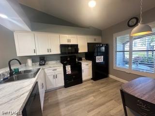 kitchen featuring lofted ceiling, pendant lighting, black appliances, sink, and white cabinetry