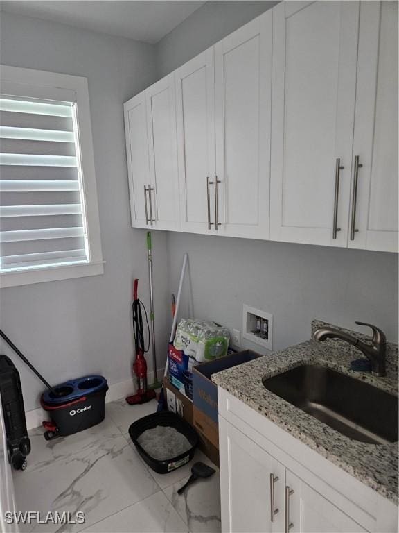 clothes washing area with cabinet space, baseboards, marble finish floor, washer hookup, and a sink