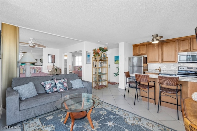 living room featuring ceiling fan, sink, light tile patterned floors, and a textured ceiling