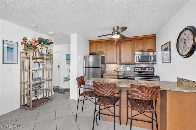 kitchen featuring a kitchen breakfast bar, kitchen peninsula, stainless steel appliances, and a textured ceiling