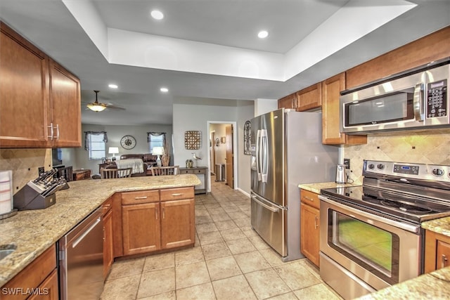 kitchen with ceiling fan, light stone countertops, stainless steel appliances, and tasteful backsplash