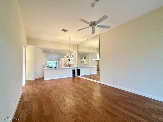 unfurnished living room with wood-type flooring and ceiling fan with notable chandelier