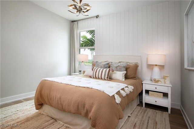 bedroom with hardwood / wood-style flooring, wooden walls, and a chandelier