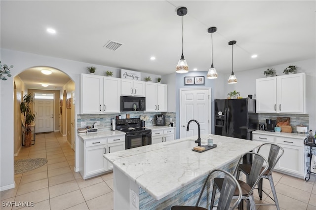 kitchen with black appliances, white cabinets, decorative backsplash, light stone countertops, and an island with sink