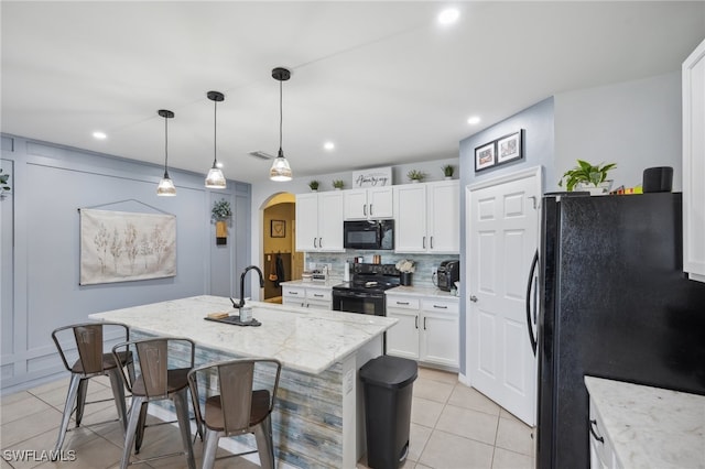 kitchen featuring a center island with sink, white cabinets, black appliances, and decorative light fixtures