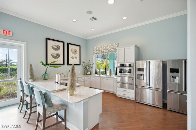 kitchen with a healthy amount of sunlight, hardwood / wood-style floors, white cabinets, and stainless steel appliances