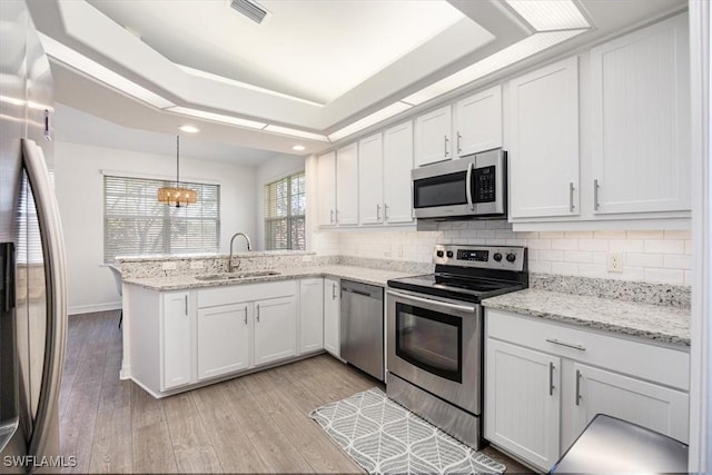 kitchen with appliances with stainless steel finishes, white cabinetry, hanging light fixtures, and sink