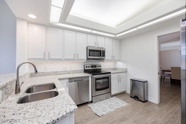 kitchen featuring white cabinets, sink, light hardwood / wood-style floors, light stone counters, and stainless steel appliances