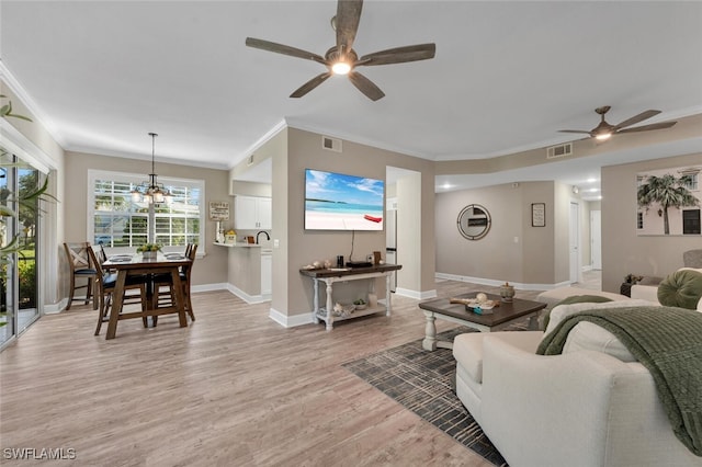 living room with crown molding, ceiling fan with notable chandelier, and light hardwood / wood-style flooring