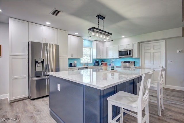 kitchen with pendant lighting, white cabinets, light stone countertops, light wood-type flooring, and stainless steel appliances