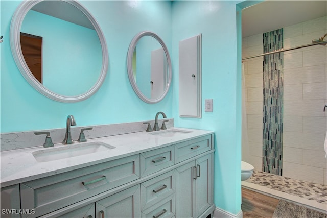 bathroom featuring a tile shower, hardwood / wood-style floors, vanity, and toilet