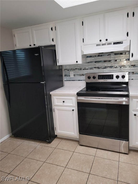 kitchen with light tile patterned floors, decorative backsplash, white cabinets, black fridge, and electric stove