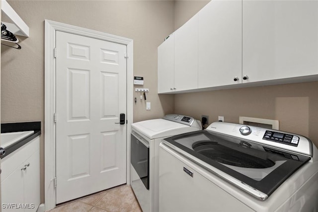 clothes washing area with cabinets, light tile patterned floors, and washer and dryer