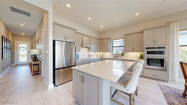 kitchen with premium range hood, stainless steel appliances, a breakfast bar, a kitchen island, and gray cabinetry