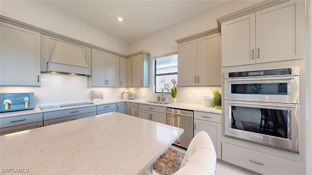 kitchen featuring stainless steel appliances, premium range hood, gray cabinets, and sink