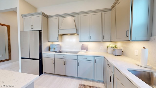 kitchen with custom exhaust hood, gray cabinetry, black electric stovetop, fridge, and backsplash