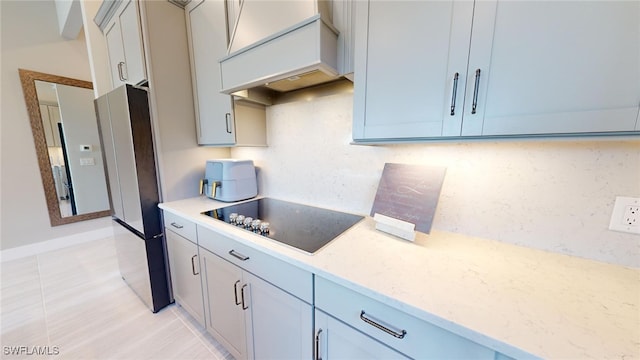 kitchen with fridge, light stone counters, custom range hood, backsplash, and black electric stovetop