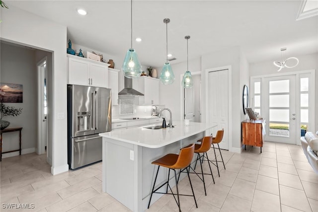 kitchen with high end refrigerator, a kitchen island with sink, sink, pendant lighting, and white cabinets