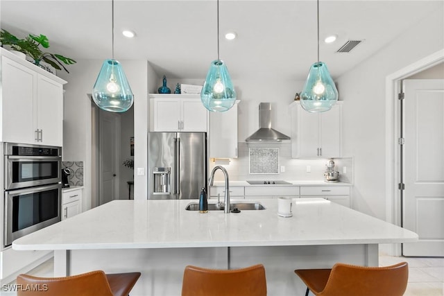 kitchen with appliances with stainless steel finishes, an island with sink, wall chimney exhaust hood, and sink