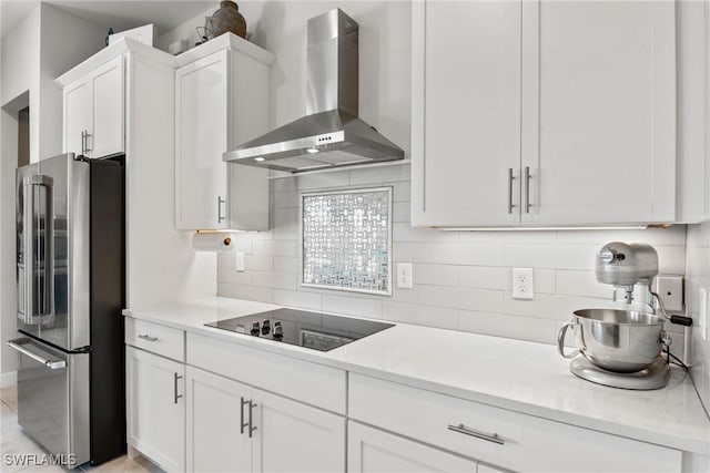 kitchen with decorative backsplash, white cabinetry, high end fridge, and wall chimney range hood