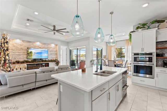 kitchen featuring a center island with sink, a raised ceiling, white cabinets, and sink