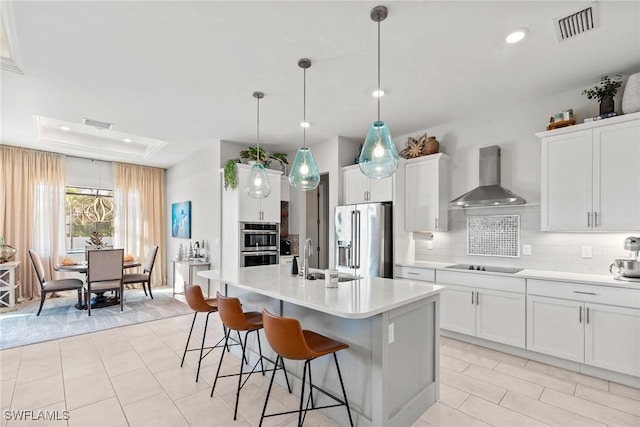 kitchen with sink, hanging light fixtures, stainless steel appliances, wall chimney range hood, and a center island with sink