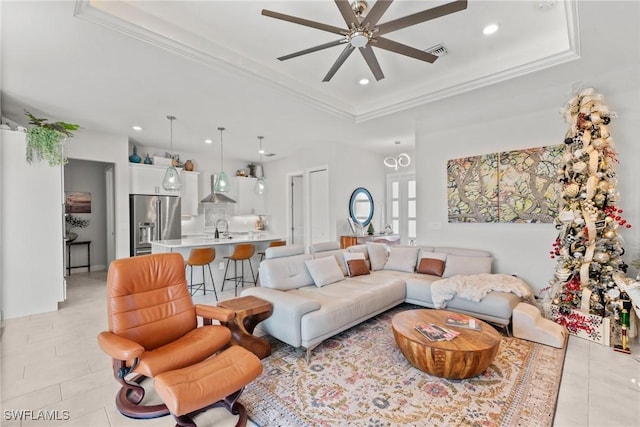 tiled living room featuring ceiling fan, crown molding, sink, and a tray ceiling