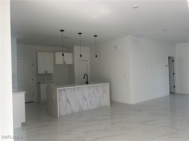 kitchen featuring a kitchen island with sink, white cabinets, sink, decorative backsplash, and decorative light fixtures