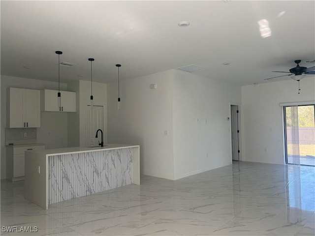 kitchen featuring ceiling fan, sink, decorative light fixtures, a center island with sink, and white cabinetry