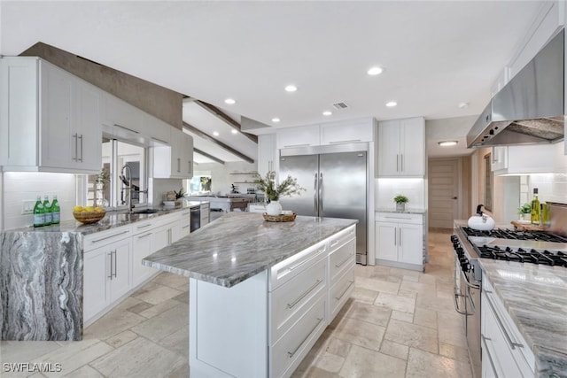 kitchen featuring white cabinets, premium appliances, light stone counters, and extractor fan