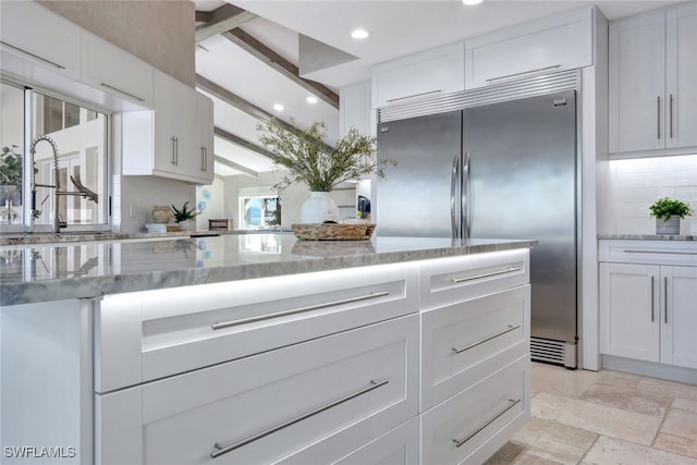 kitchen with beam ceiling, white cabinetry, light stone countertops, and built in fridge