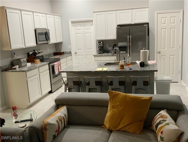 kitchen with light stone countertops, appliances with stainless steel finishes, sink, white cabinets, and an island with sink